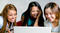 Three girls gathered around a laptop.