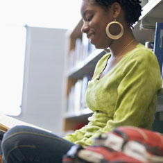 A girl leaning against a bookcase and reading
