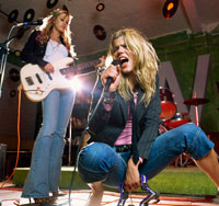 Two girls singing loudly and playing guitar.