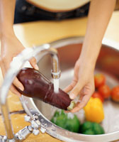 Woman washing vegetables in a sink.