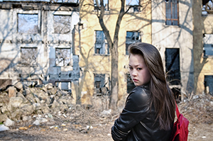 A girl outside alone in an area ravaged by disaster.